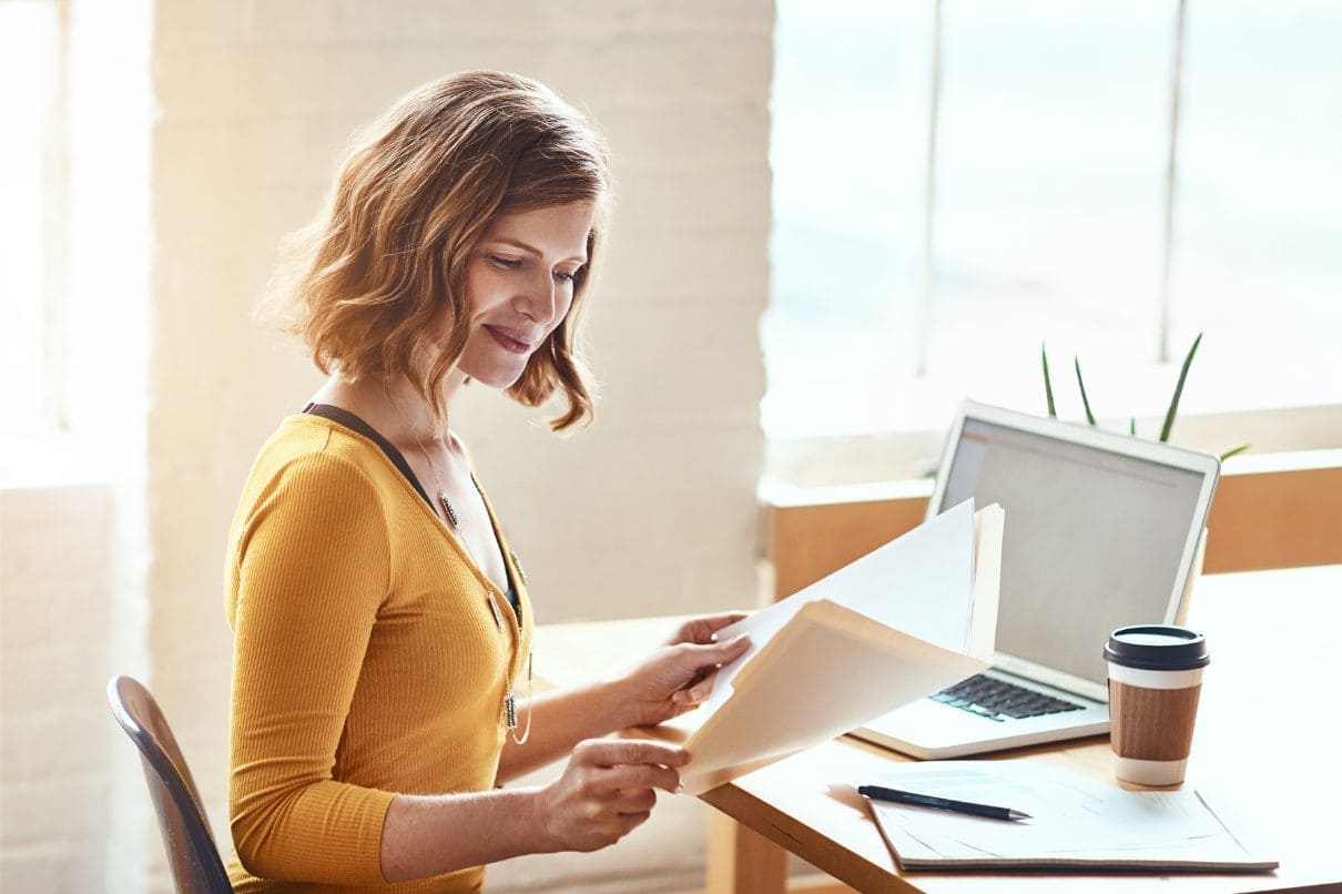 A woman working at a desk with a laptop and papers spread out in front of her